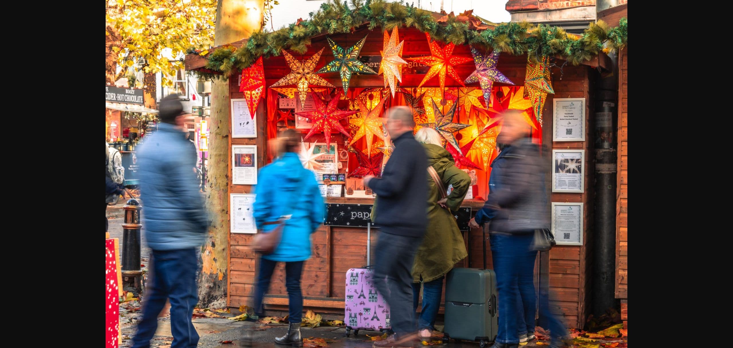 Shoppers browsing an illuminated paper-star stall at York Christmas Market. Source: https://www.makeityork.com/uncategorized/2025/11/photo-story-york-christmas-market-festivities-return-to-york-today/