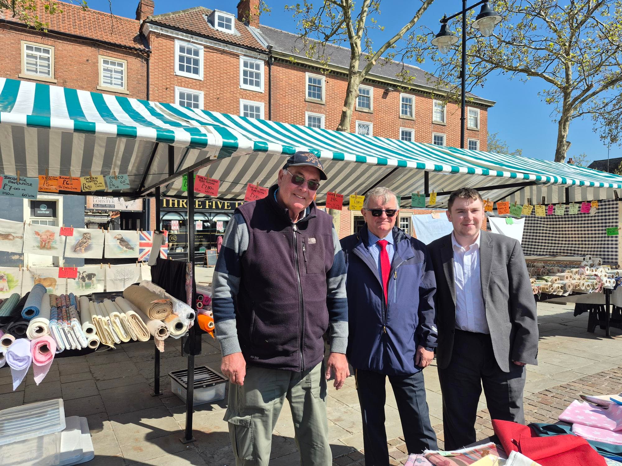 A Retford Market trader and councillors in front of the market's green-and-white stalls. Source: https://www.bassetlaw.gov.uk/media-centre/news/news-archive/news-may-2026/new-stalls-smarten-up-retford-market/