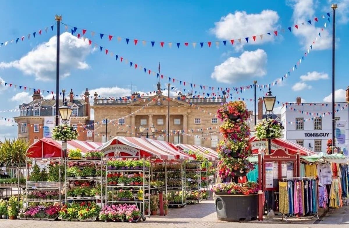 Newark Royal Market stalls with flowers, clothing and the Town Hall behind Source: https://www.newark.gov.uk/wp-content/uploads/sites/87/2024/07/302329383_498913625570873_4411574111483846608_n.jpg