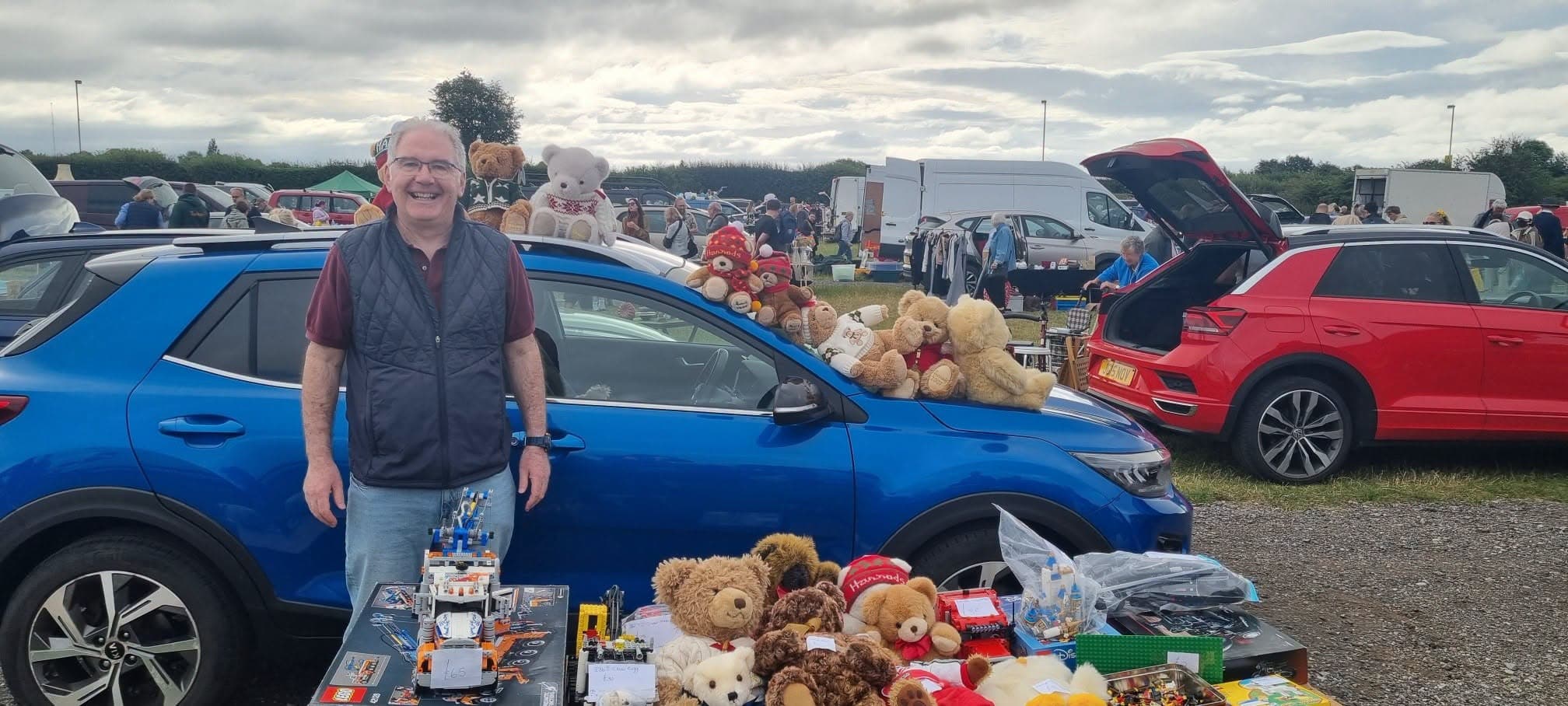 A seller with toys and teddy bears beside cars at York Racecourse Car Boot