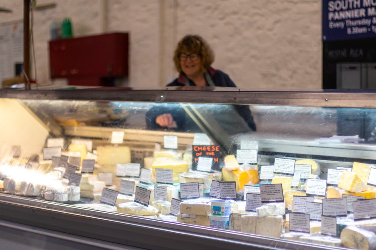 A cheese trader serving customers inside South Molton Pannier Market. Source: https://southmoltonpanniermarket.co.uk/