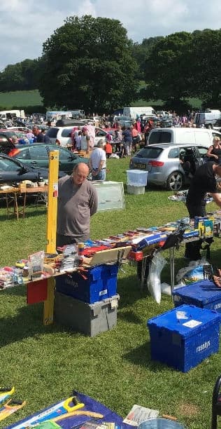 Shoppers and sellers among cars and tables at Big Ben's West Wycombe car boot. Source: https://static.wixstatic.com/media/a471b2_cfda03b41c524d6a91d0e171e10d4589~mv2.jpg/v1/fill/w_316,h_612,al_c,q_80,enc_avif,quality_auto/a471b2_cfda03b41c524d6a91d0e171e10d4589~mv2.jpg