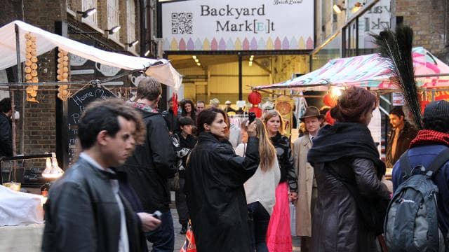 Shoppers browsing colourful stalls at Backyard Market, part of Brick Lane Market. Visit London; image courtesy of Brick Lane Market. Source: https://www.visitlondon.com/things-to-do/place/279336-brick-lane-market