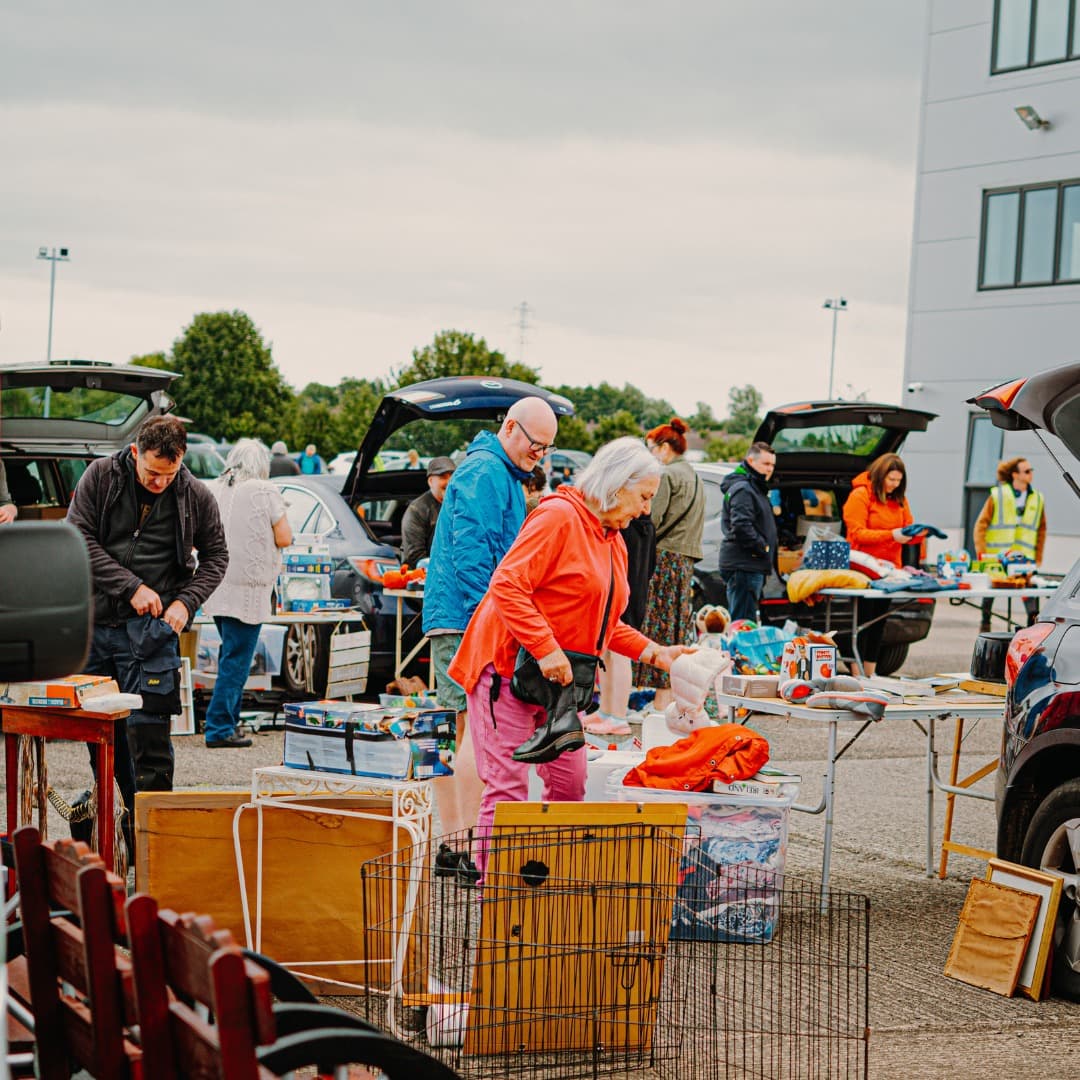 Shoppers browsing second-hand goods beside cars at Vineyard Market in Coleraine Source: https://market.vineyardcompassion.co.uk/assets/market-2-46603bc3fdd2b65d4d47b64ad00c63e2135c780ca28d3d24f97b76eb55f8128c.jpg