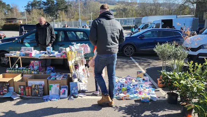 A shopper browsing an exact Dorking Car Boot Sale pitch on the station-side hardstanding, with cars and more stalls behind. Source: https://www.google.com/maps/place/Dorking+Car+Boot+Sale/data=!4m2!3m1!1s0x0:0x50ad6d98714eaea8