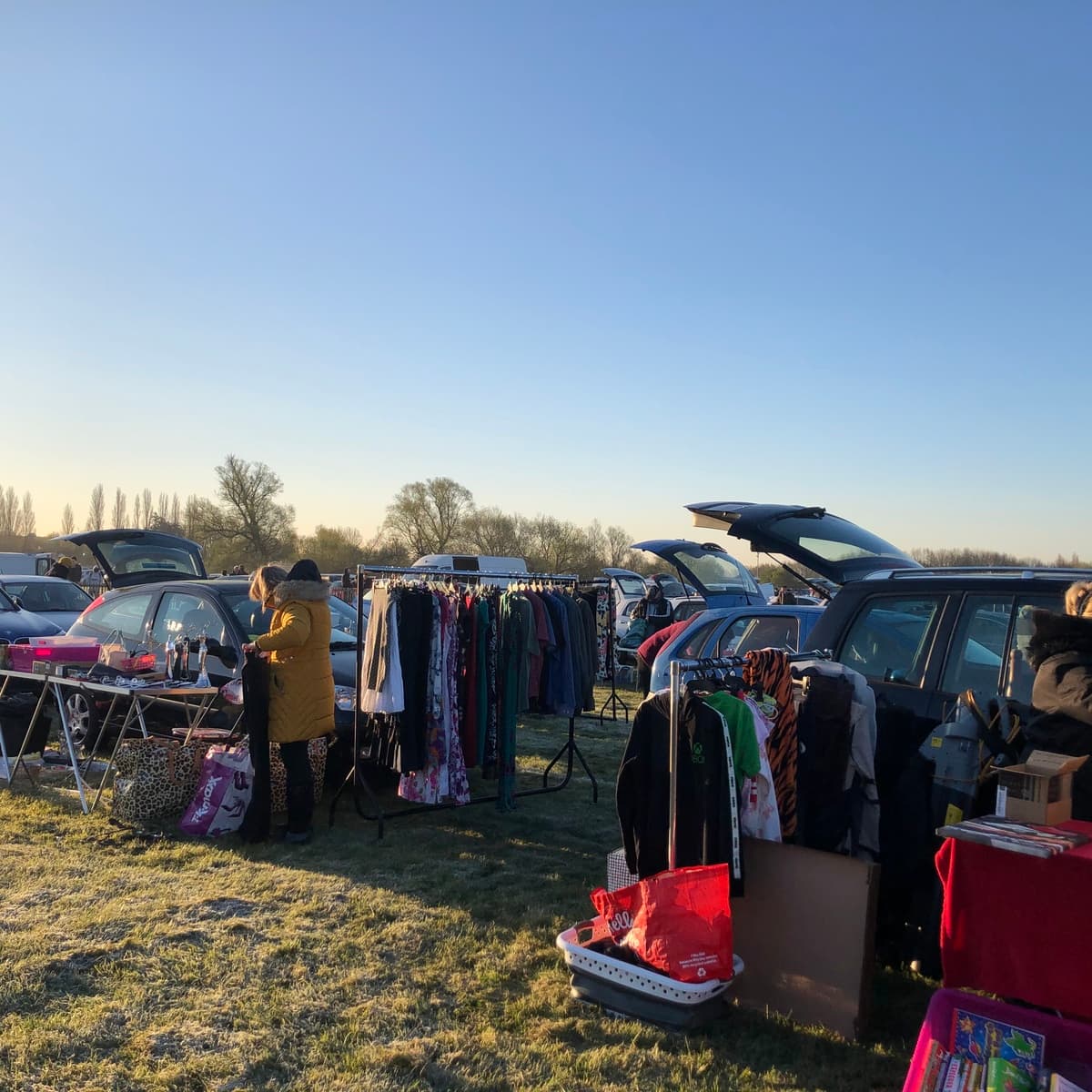 Shoppers browsing clothes beside open car boots at Shepperton Source: https://www.sheppertoncarboot.co.uk/assets/img/large_B486E3F3-F973-4F63-AC44-772171F21269.jpeg