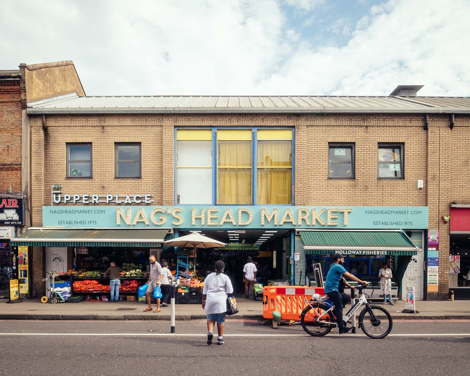 Shoppers outside the signed Nag's Head Market entrance on Seven Sisters Road. Source: https://nagsheadmarket.com/wp-content/uploads/2024/02/NagsHead-JimStephenson-1-WebRes.jpg