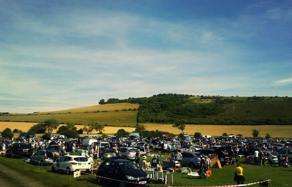 Wide view of Shoreham Flyover Car Boot with rows of seller vehicles and shoppers beneath the South Downs Source: https://www.findcarboot.co.uk/shoreham-flyover-car-boot-sale/
