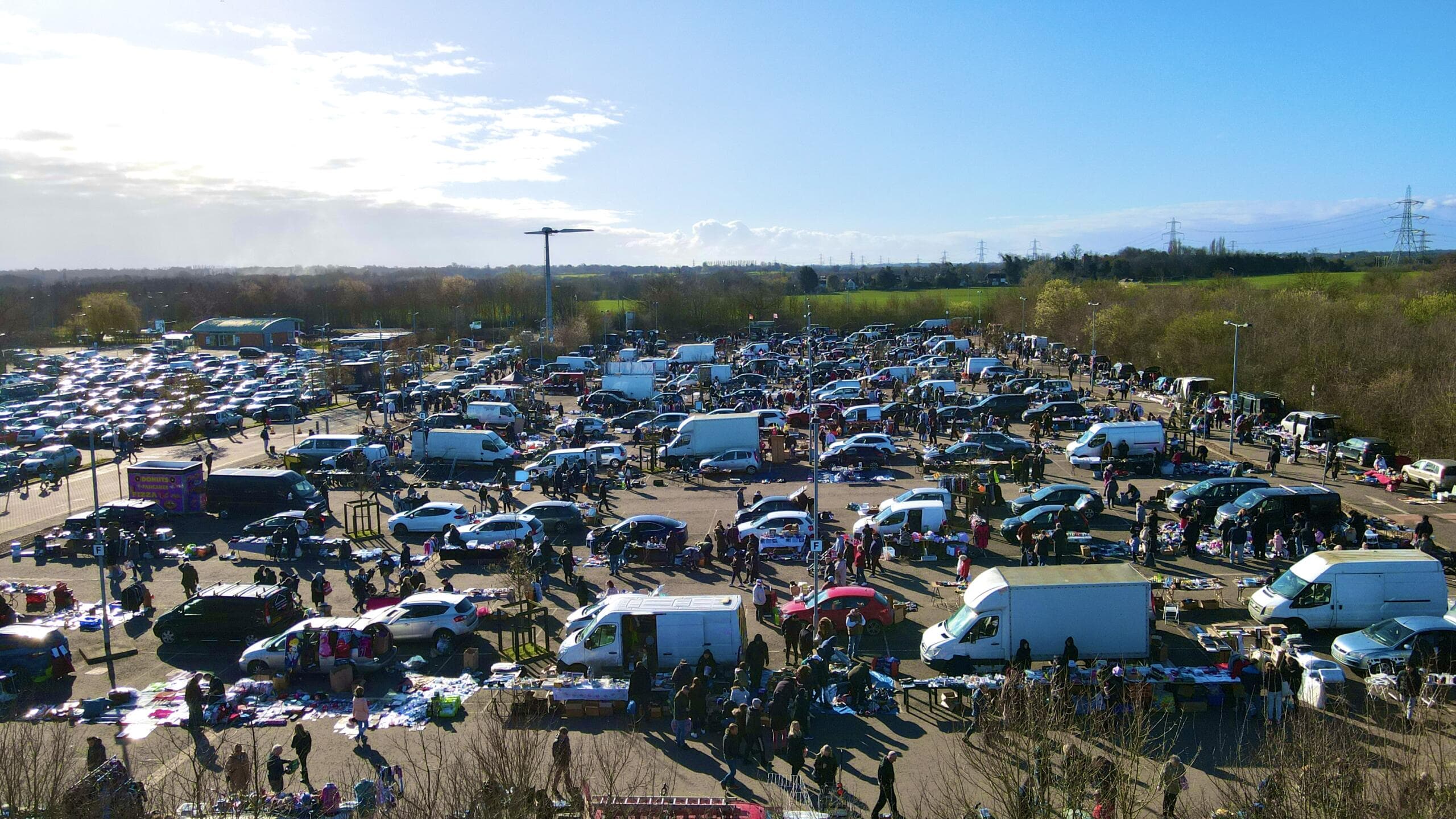 Chelmsford Sandon Car Boot Sale with cars, stalls and shoppers across the hardstanding. Source: https://capitalbootsales.co.uk/app/uploads/2023/01/dji-fly-20230226-100446-187-1677405896088-photo-scaled-1.jpg