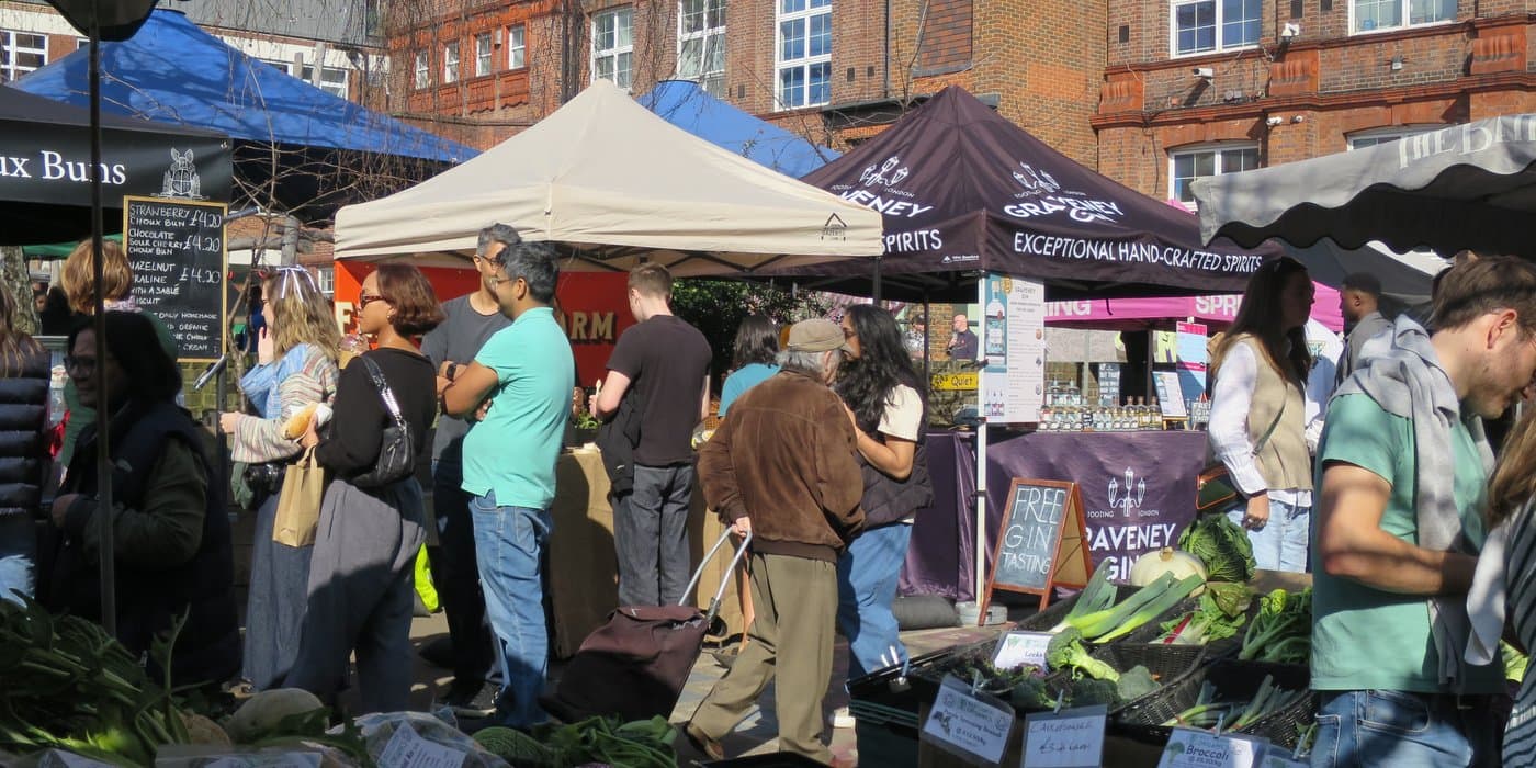 Shoppers browsing produce and food stalls at Queen's Park Farmers' Market. Source: https://www.lfm.org.uk/markets/queens-park/