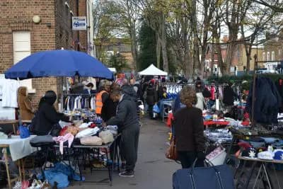 Tottenham Car Boot Sale with tables of goods, sellers and shoppers. Source: https://www.countrysidepromotions.co.uk/wp-content/uploads/2022/01/Tottenham-car-boot-sale-400x267.jpg.webp
